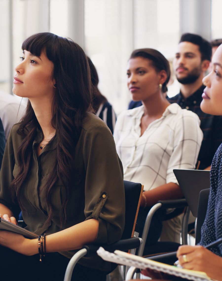 Teilnehmende einer Security-Awareness-Schulung sitzen aufmerksam in einem Seminarraum und machen sich Notizen.