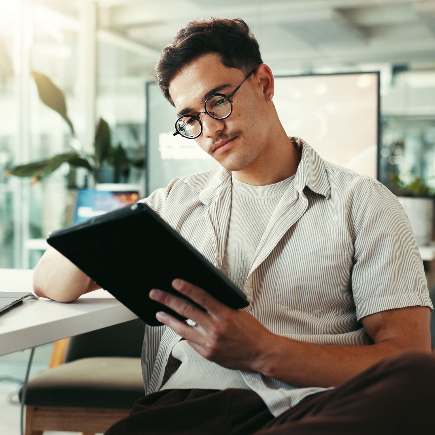 Ein Mitarbeiter sitzt im Büro und nutzt ein Tablet zur Verwaltung von Netzwerkzugängen und IT-Sicherheitsrichtlinien.
