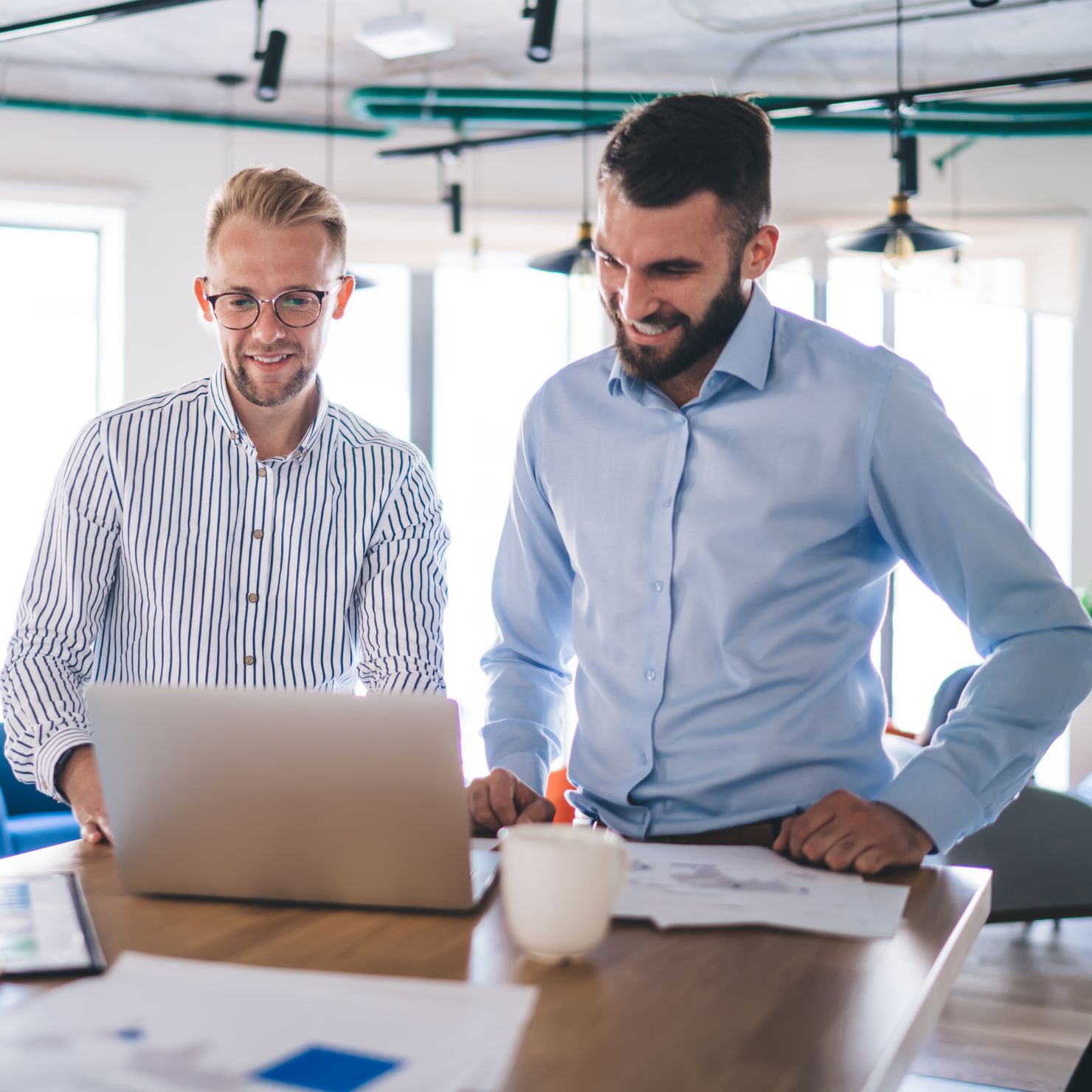 Zwei Mitarbeiter besprechen am Laptop IT-Sicherheitszertifizierungen und Audits zur Verbesserung von Compliance und Informationssicherheit im Unternehmen.