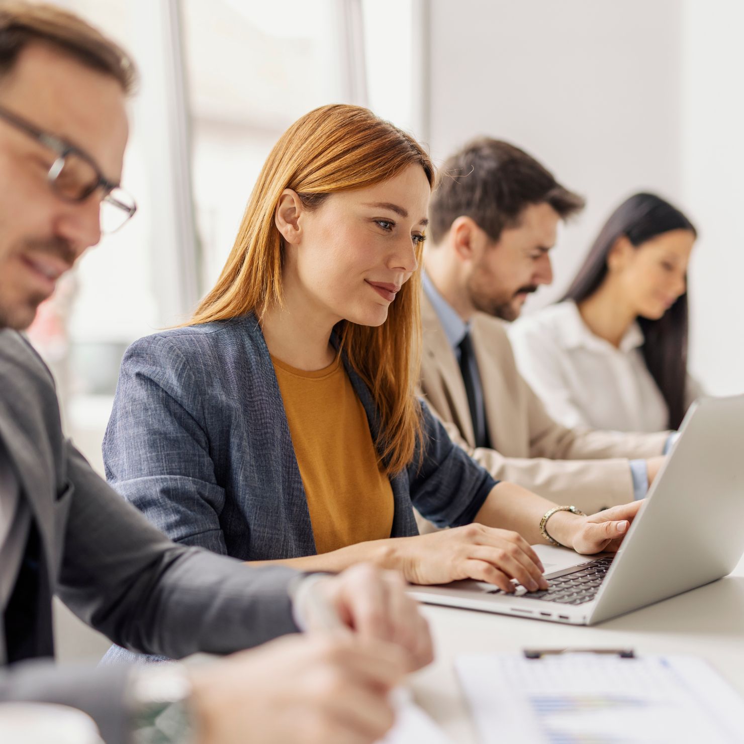 Mehrere Mitarbeitende arbeiten in einer Besprechung mit Laptop zusammen und besprechen digitale Prozesse im Unternehmen.