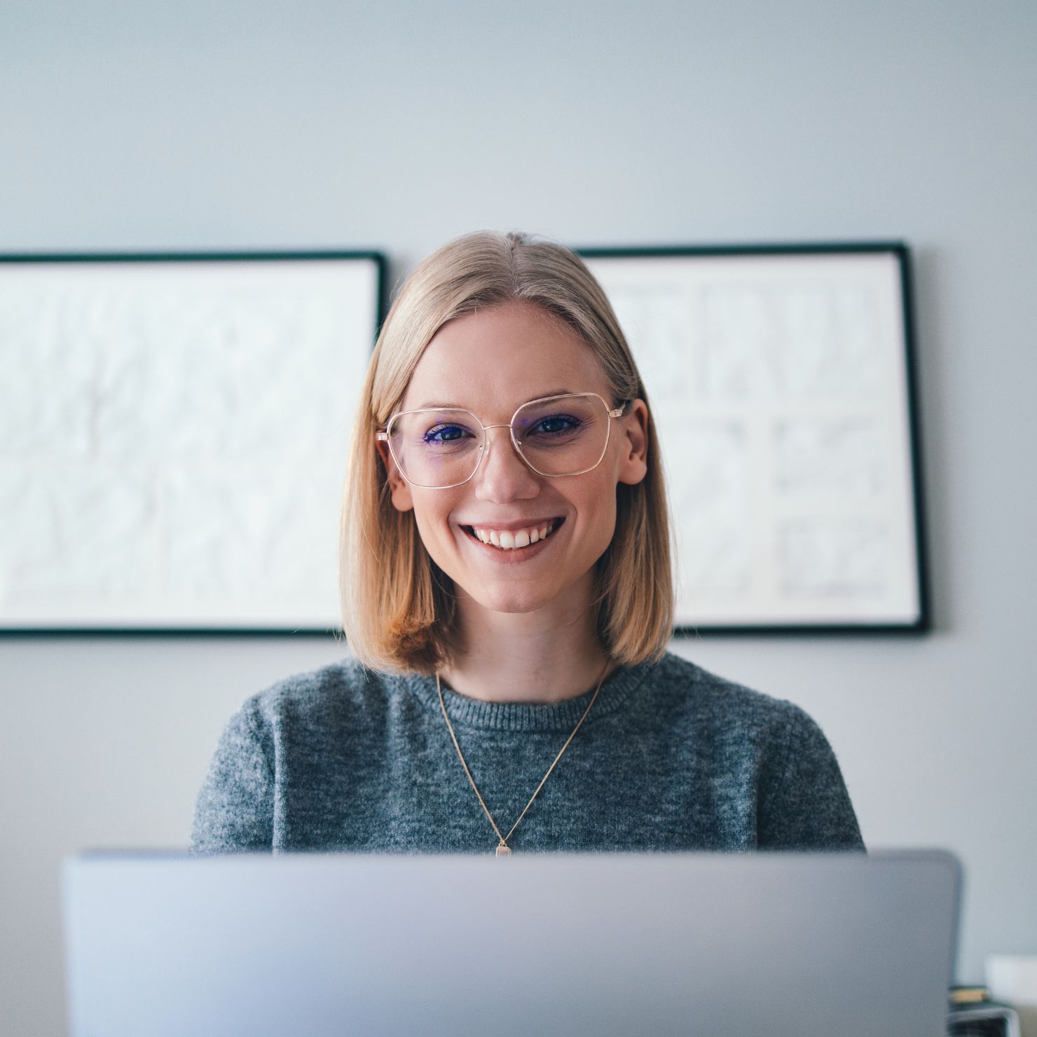 Lächelnde Frau mit Brille arbeitet am Laptop.