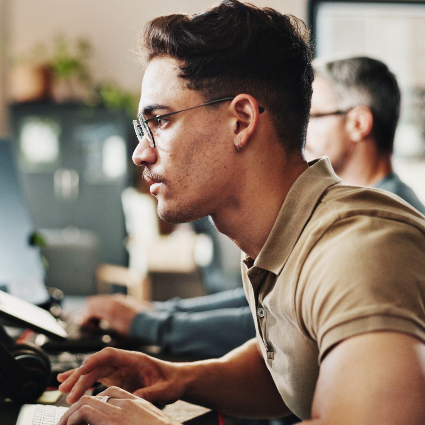 Mitarbeiter im Profil am Arbeitsplatz vor mehreren Bildschirmen, konzentriert bei der Arbeit im IT-Sicherheitsumfeld.