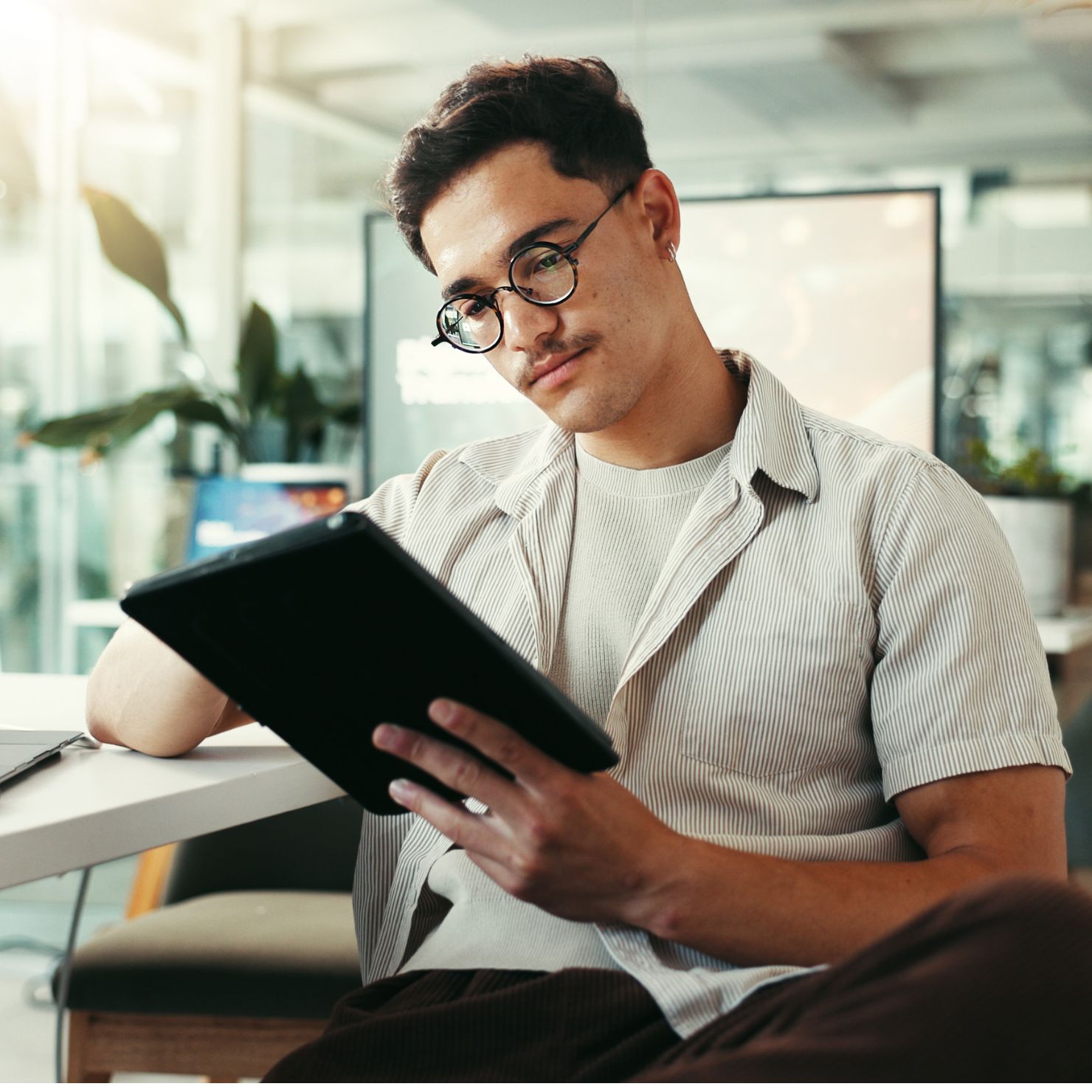 Junger IT-Sicherheitsexperte arbeitet konzentriert an einem Ipad in einer modernen Büroumgebung.