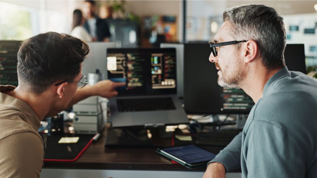Zwei Mitarbeitende von Allgeier Cyris besprechen IT-Inhalte gemeinsam vor mehreren Bildschirmen im Büro.