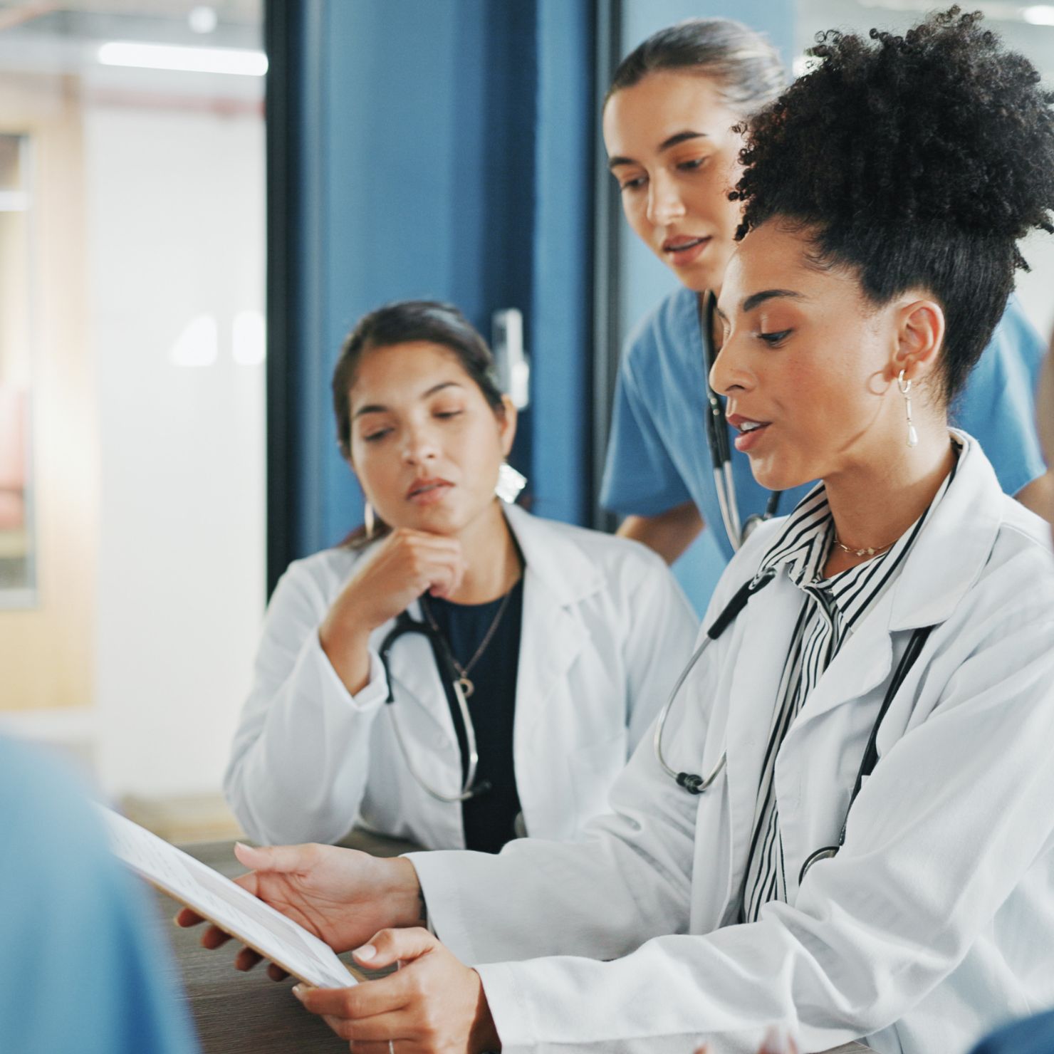 Drei medizinische Fachkräfte besprechen gemeinsam Patientenunterlagen in einer Klinik oder Praxis.