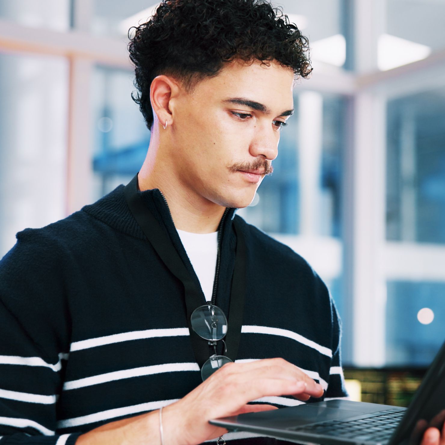 Junger Mann arbeitet mit einem Laptop und hält ein weiteres Gerät in der Hand in einer modernen Büroumgebung.