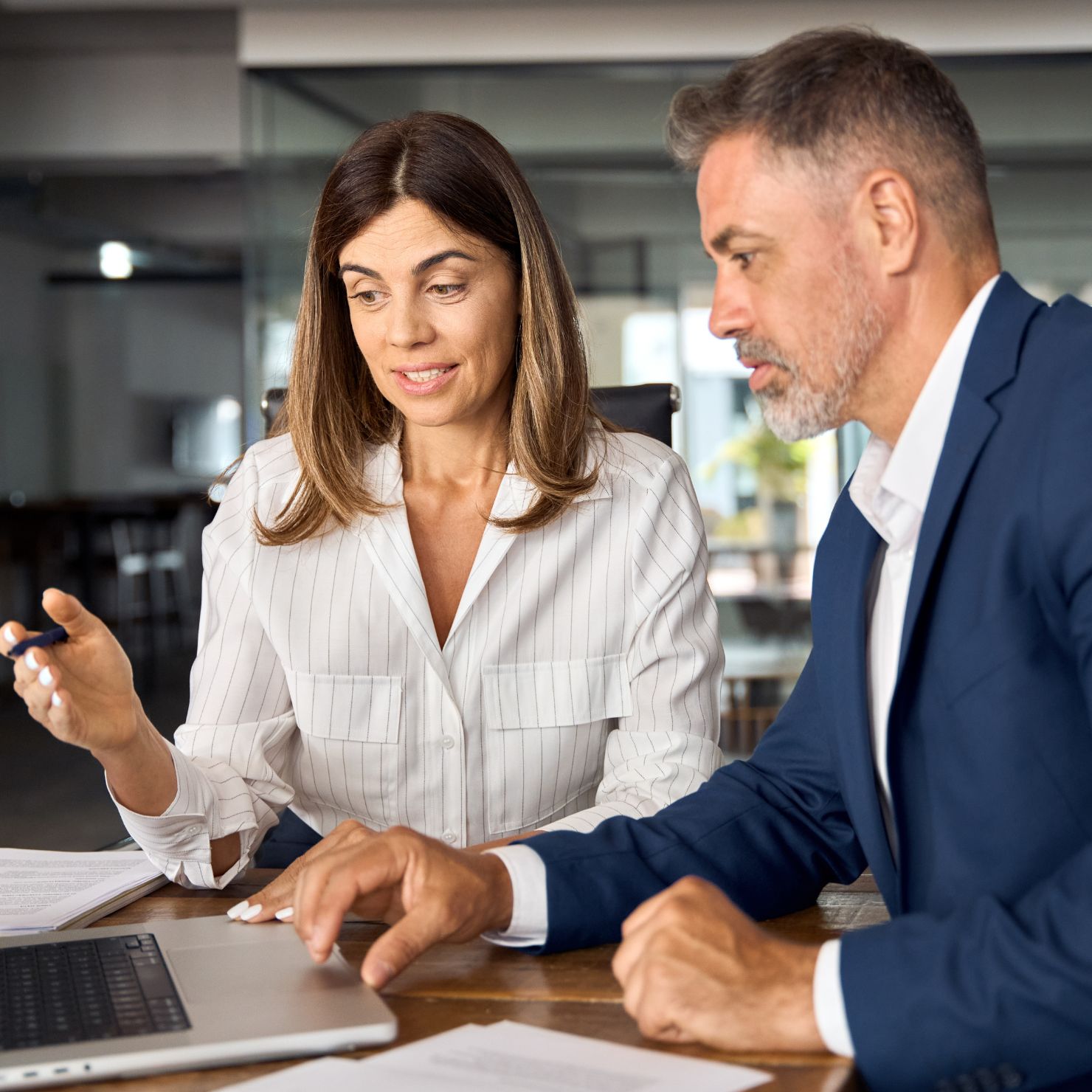 Zwei Personen im Business-Outfit besprechen gemeinsam Inhalte an einem Laptop in einem modernen Büro.