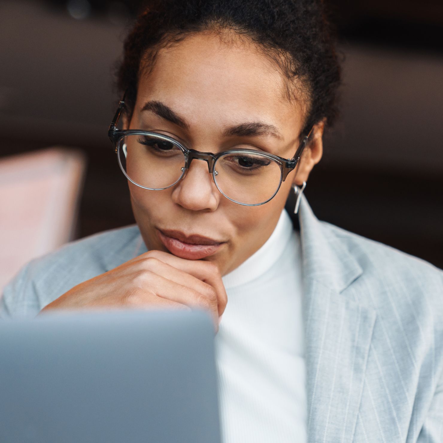 Frau mit Brille in hellem Blazer sitzt am Laptop und schaut konzentriert auf den Bildschirm.